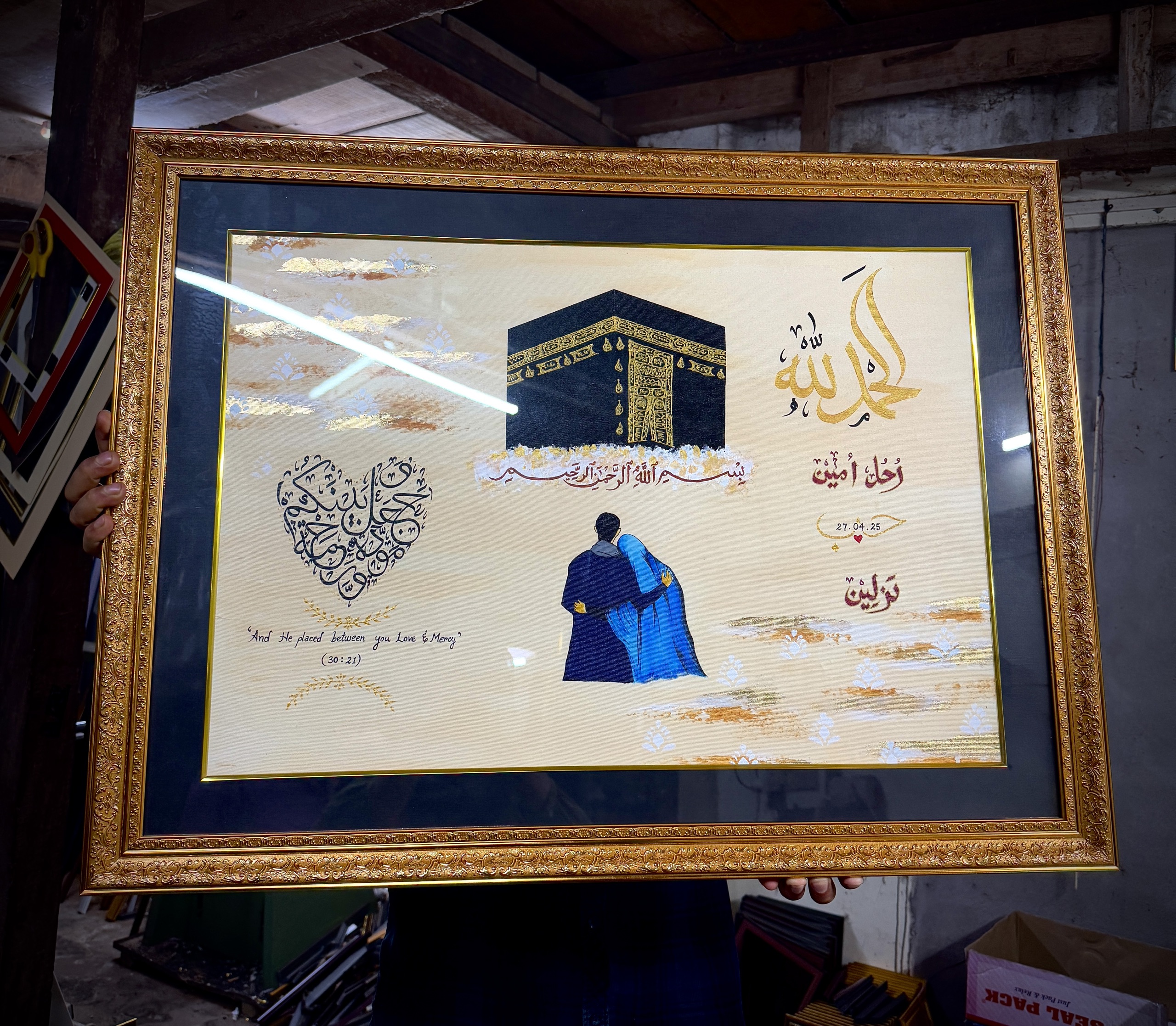 The artist holding a large gold-framed Love and Mercy commission, face hidden behind the painting