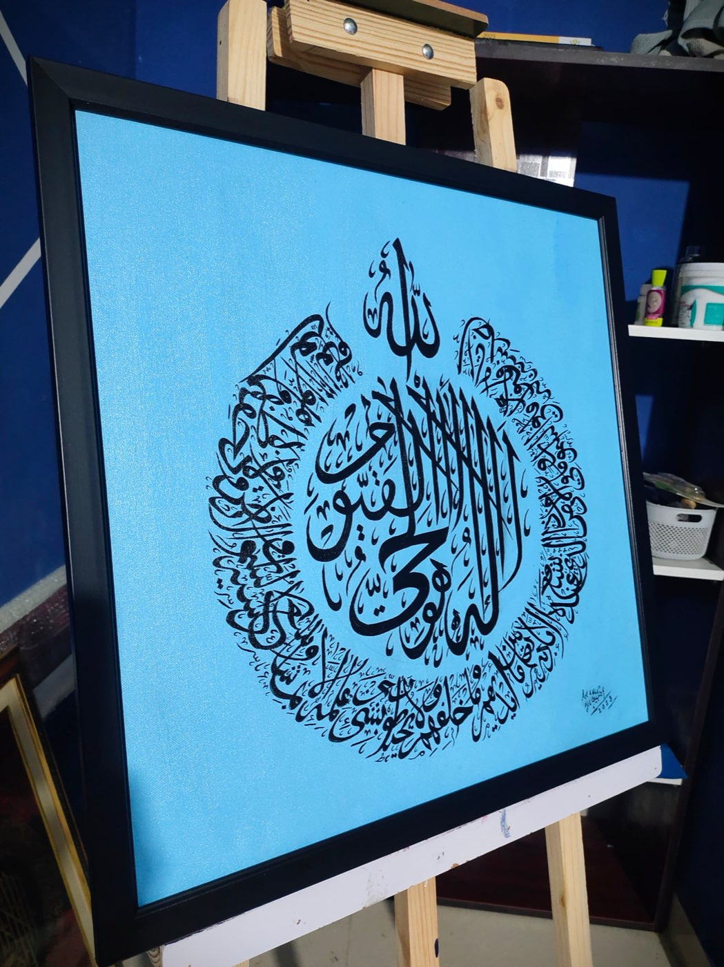 Black thuluth roundel on a sky-blue canvas in a black frame