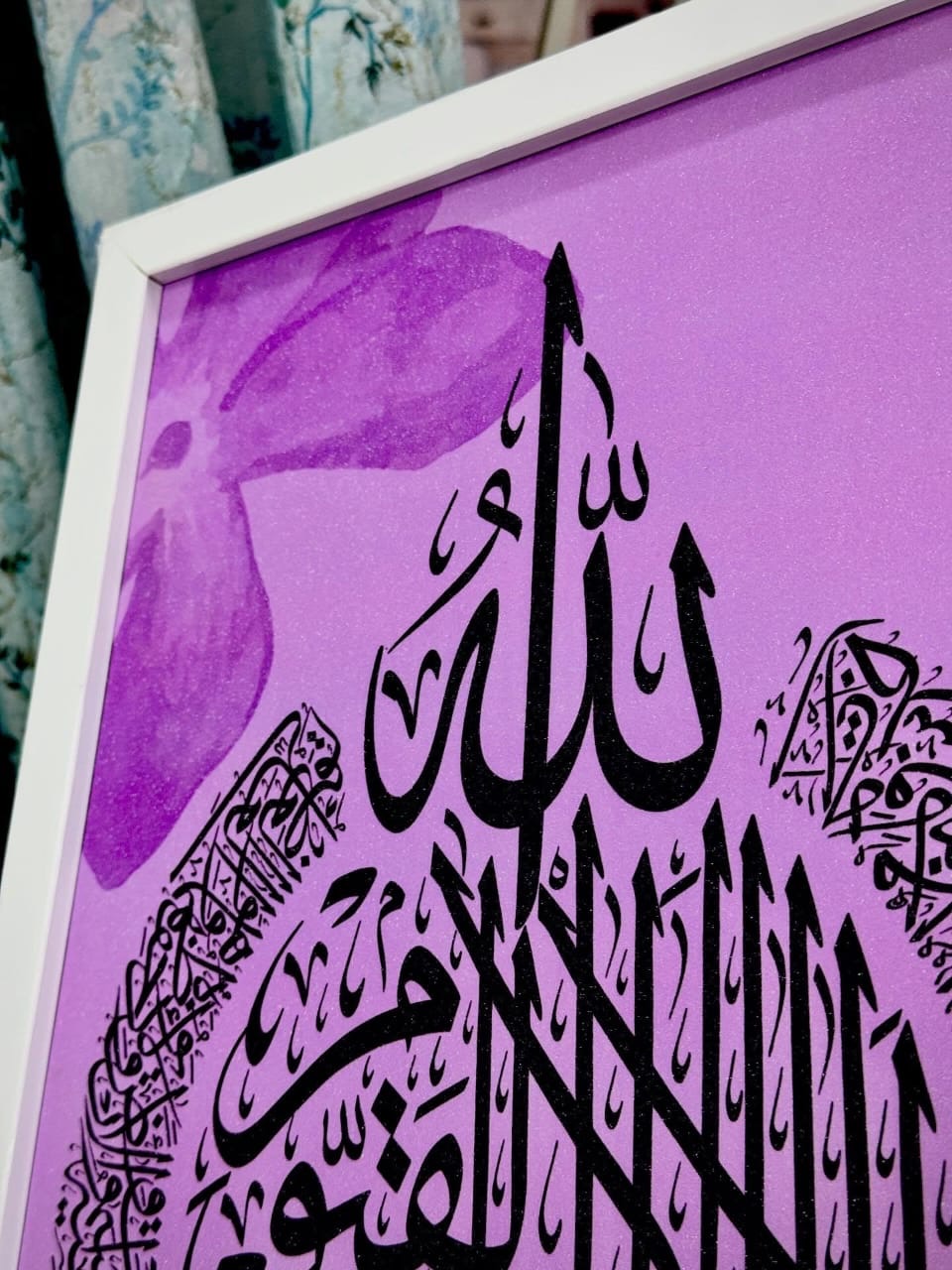 Corner detail of a lilac painting with violet blossoms behind black script, white frame
