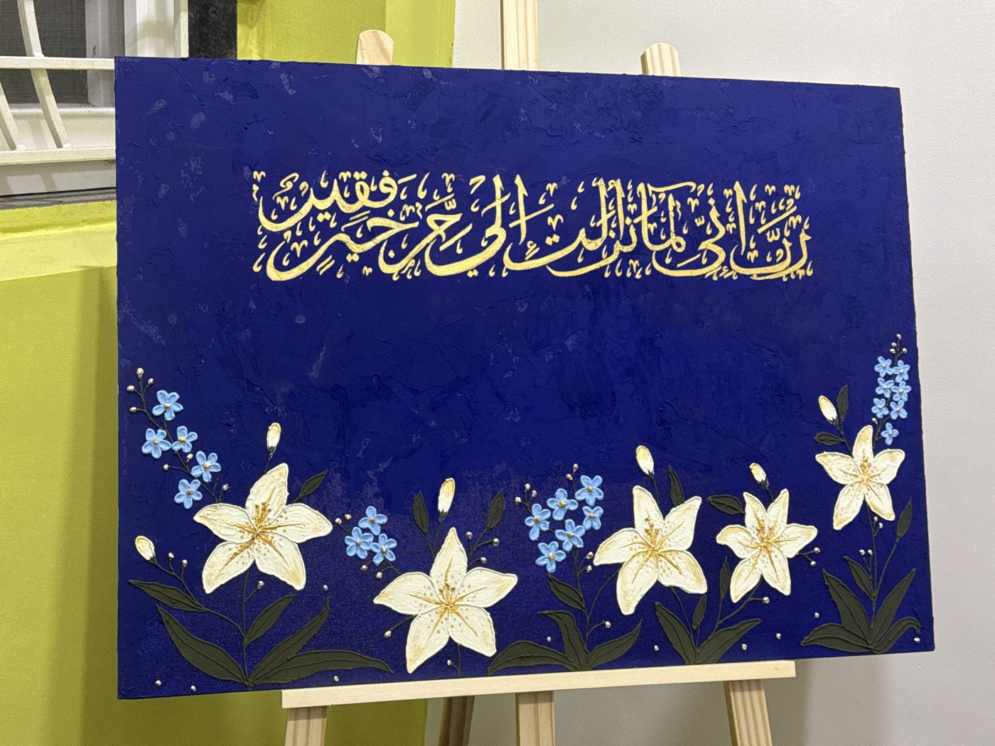 Gold calligraphy of Qur'an 28:24 on royal-blue canvas above hand-painted white lilies