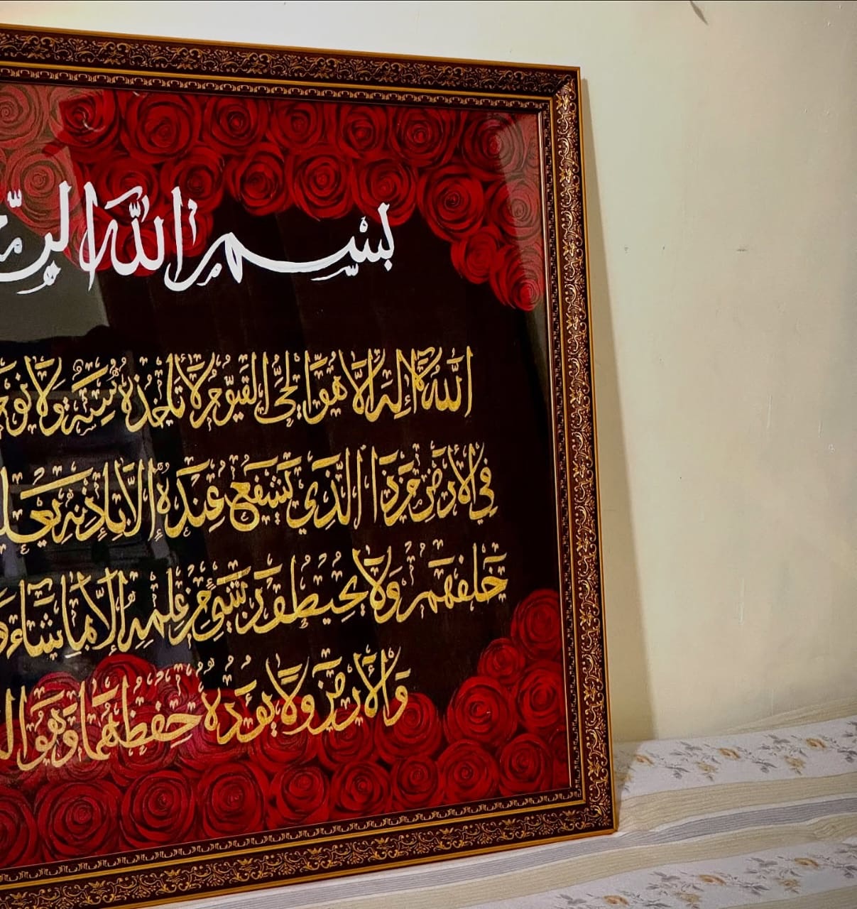 Gilded calligraphy among painted red roses in an ornate gold frame, seen at an angle