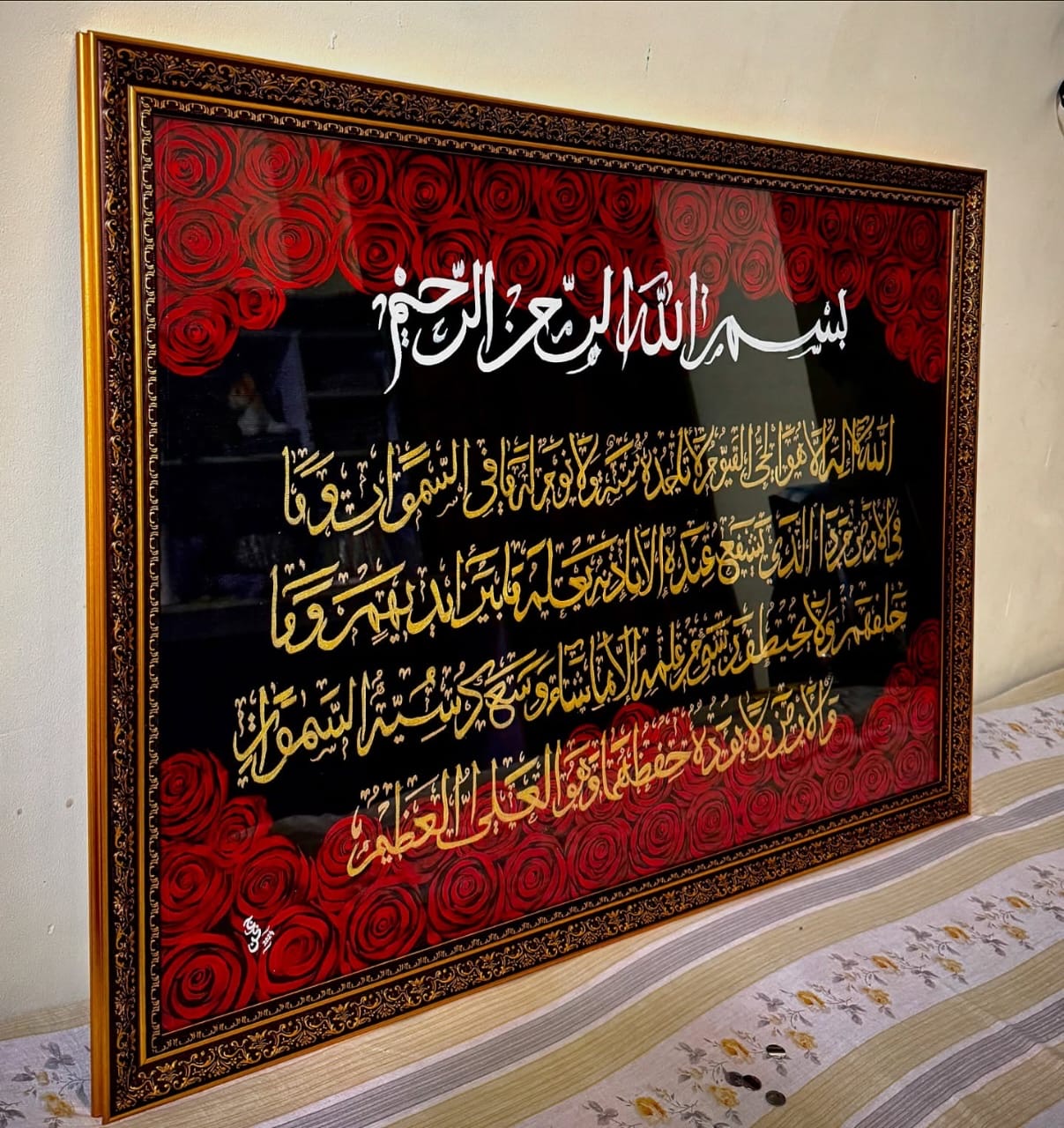 Gilded calligraphy on black surrounded by deep red roses, in an ornate gold frame