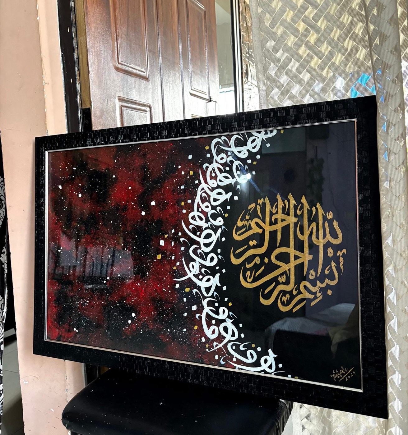 White spiral calligraphy meeting gold basmala over a red-black ground, glazed black frame