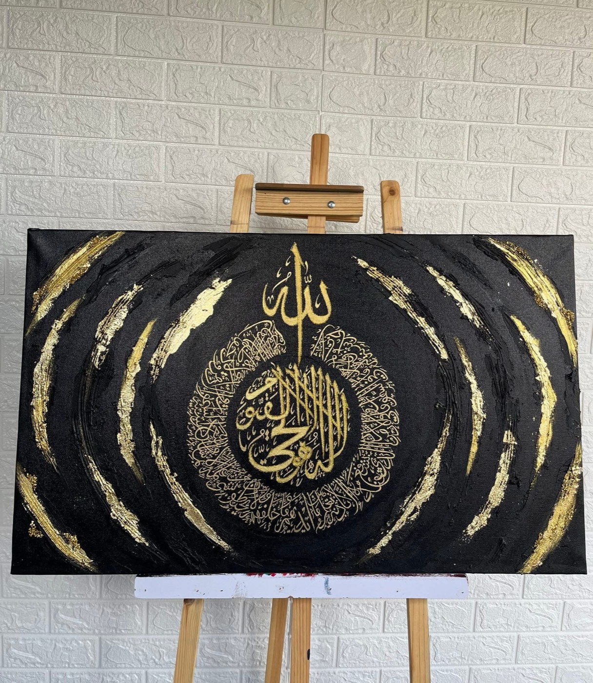 Gold calligraphy roundel with radiating gold feather strokes on black canvas on an easel