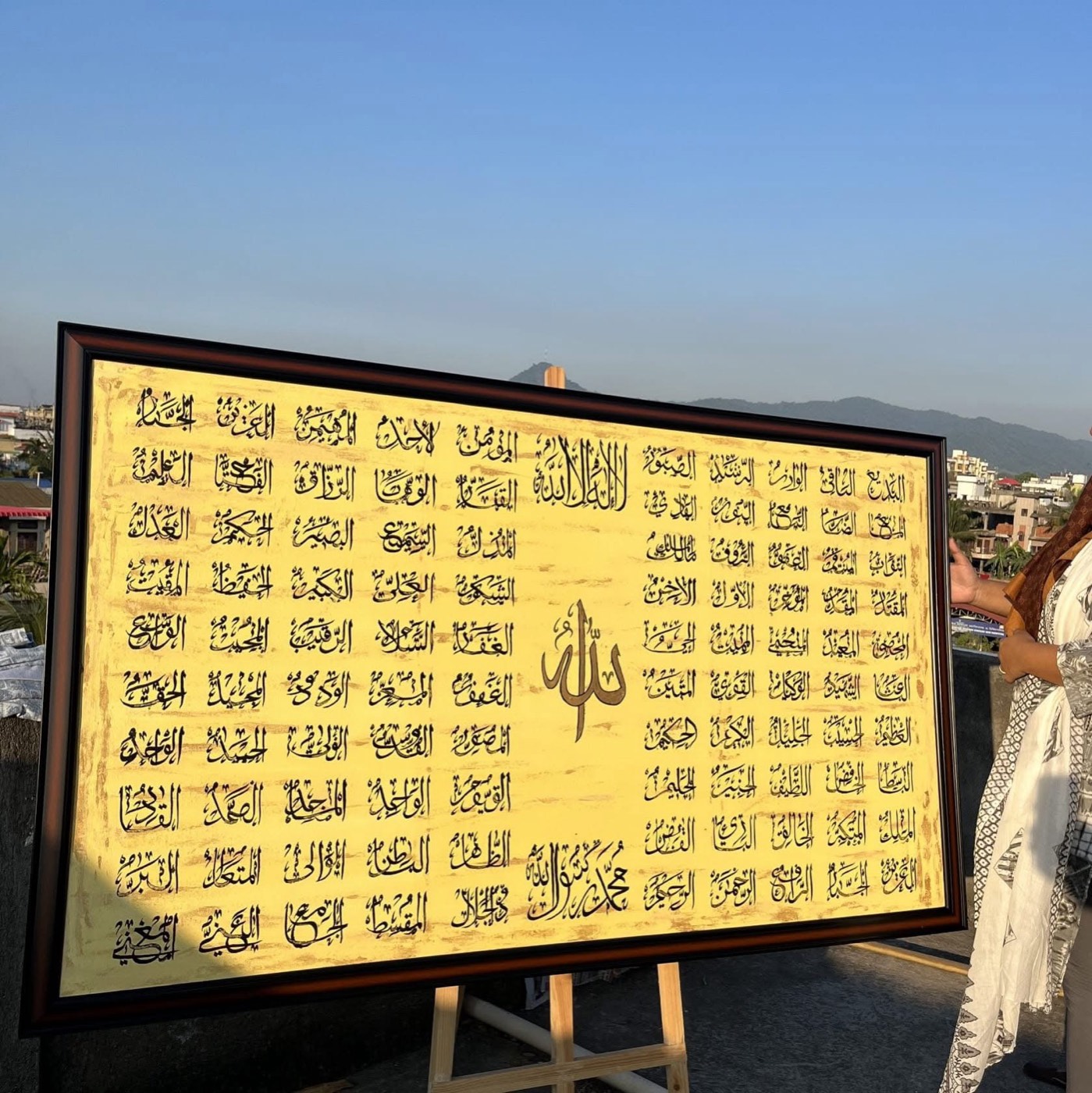 Large gold painting of the ninety-nine names of Allah in neat registers, photographed outdoors