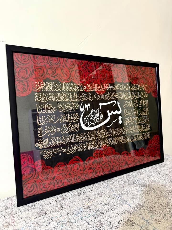 Framed piece centered on the word Ya-Sin in gold, dense gold script over black with red roses